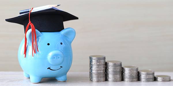 Piggy bank with graduation cap sitting next to ascending stack of coins.
